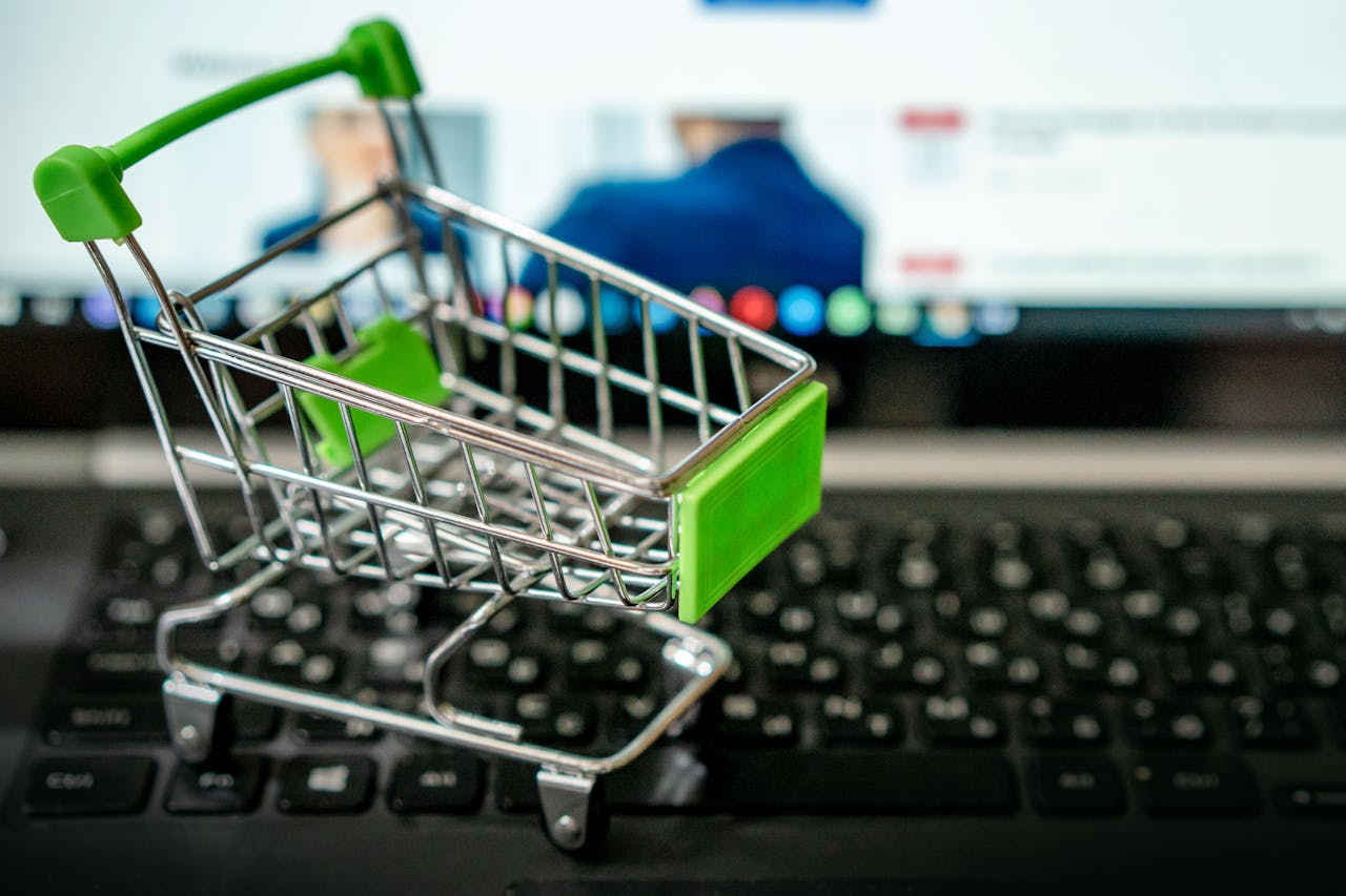 Miniaturowy koszyk zakupowy ustawiony na klawiaturze laptopa symbolizujący zakupy online