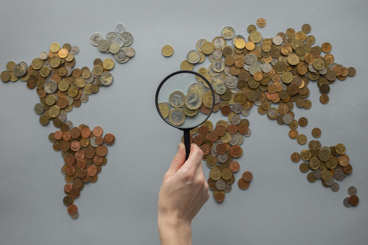 Obsługa wielu walut – mapa świata ułożona z monet i lupa symbolizująca analizę finansów