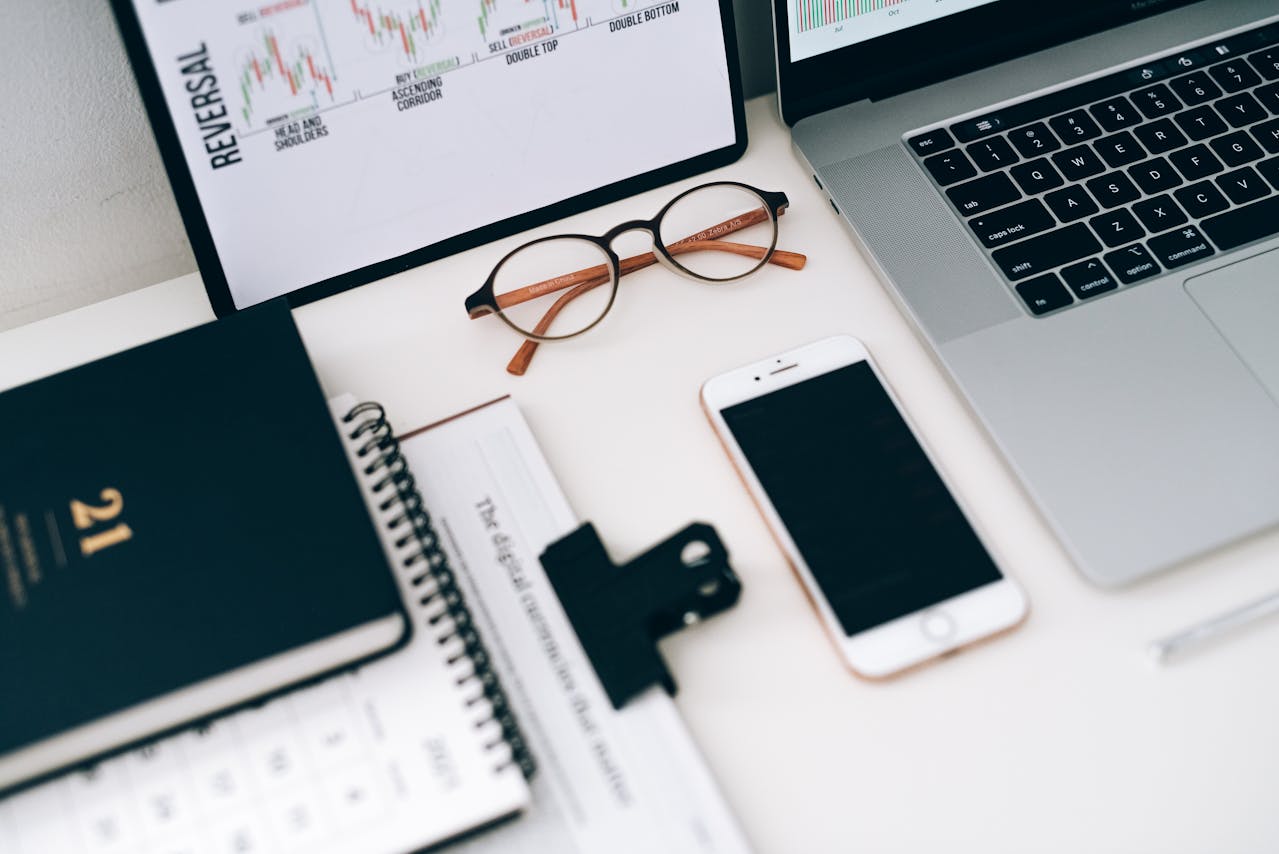 Widok biurka z laptopem, smartfonem, okularami i wykresami na ekranie – środowisko pracy analityka korzystającego z Dynamics 365 Business Central.